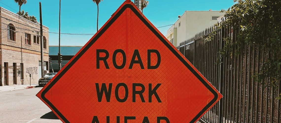 bright orange road work ahead sign with palm trees in back