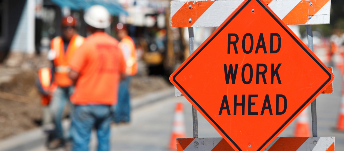 Road work ahead sign in the road with construction workers behind it.
