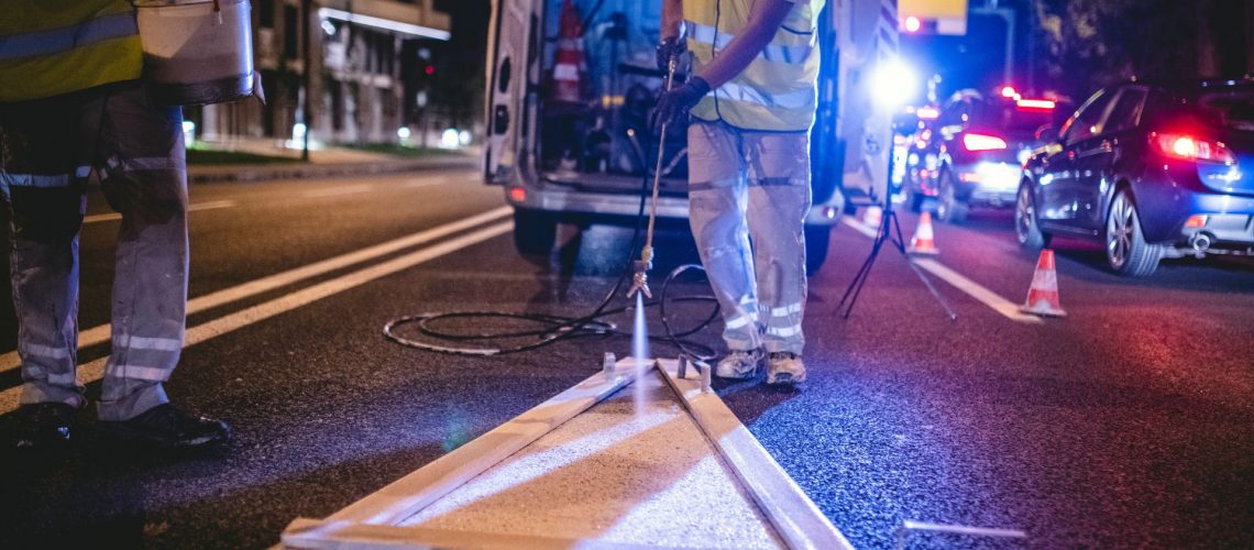 night roadworker painting road with high visibility vest on