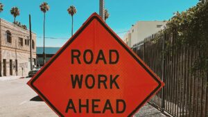 bright orange road work ahead sign with palm trees in back