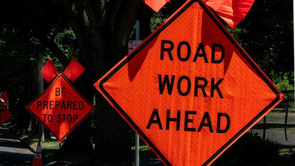 2 bright orange road work ahead signs on side of road